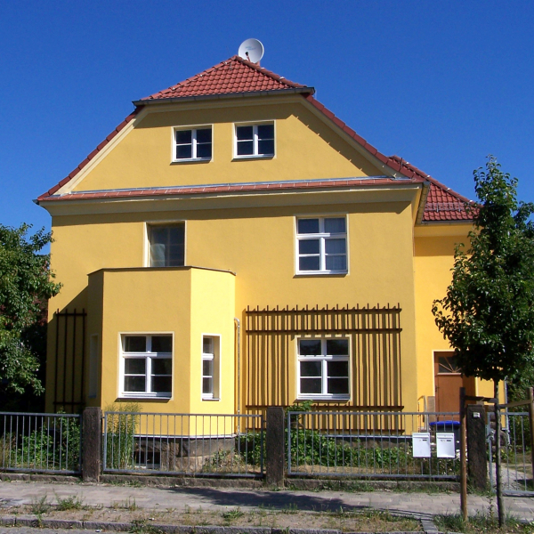 Einfamilienhaus mit Rankgitter, gelb gestrichen, rotes Ziegeldach